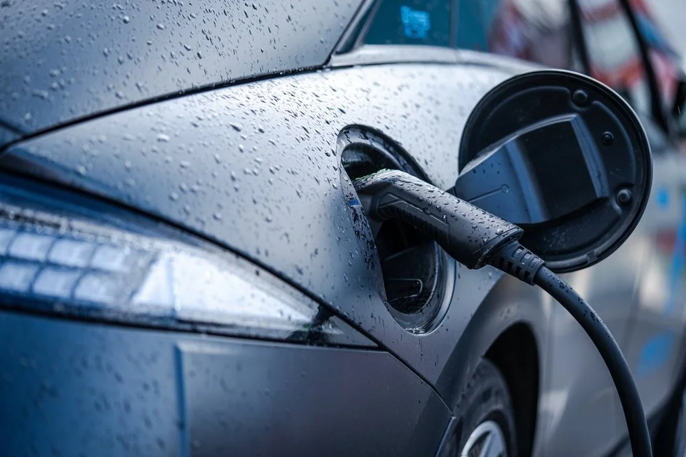 Close up shot of an electric car plugged in for charging, on a rainy day.