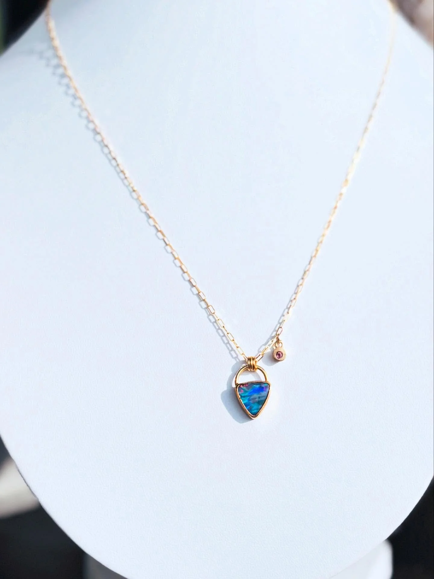 A beautiful triangular Australian Opal rests at the heart of this custom piece, its mesmerizing fire alive with flashes of color from deep within the stone. The opal is securely set in a rich 22 karat gold bezel and accented with a graceful 14 karat 