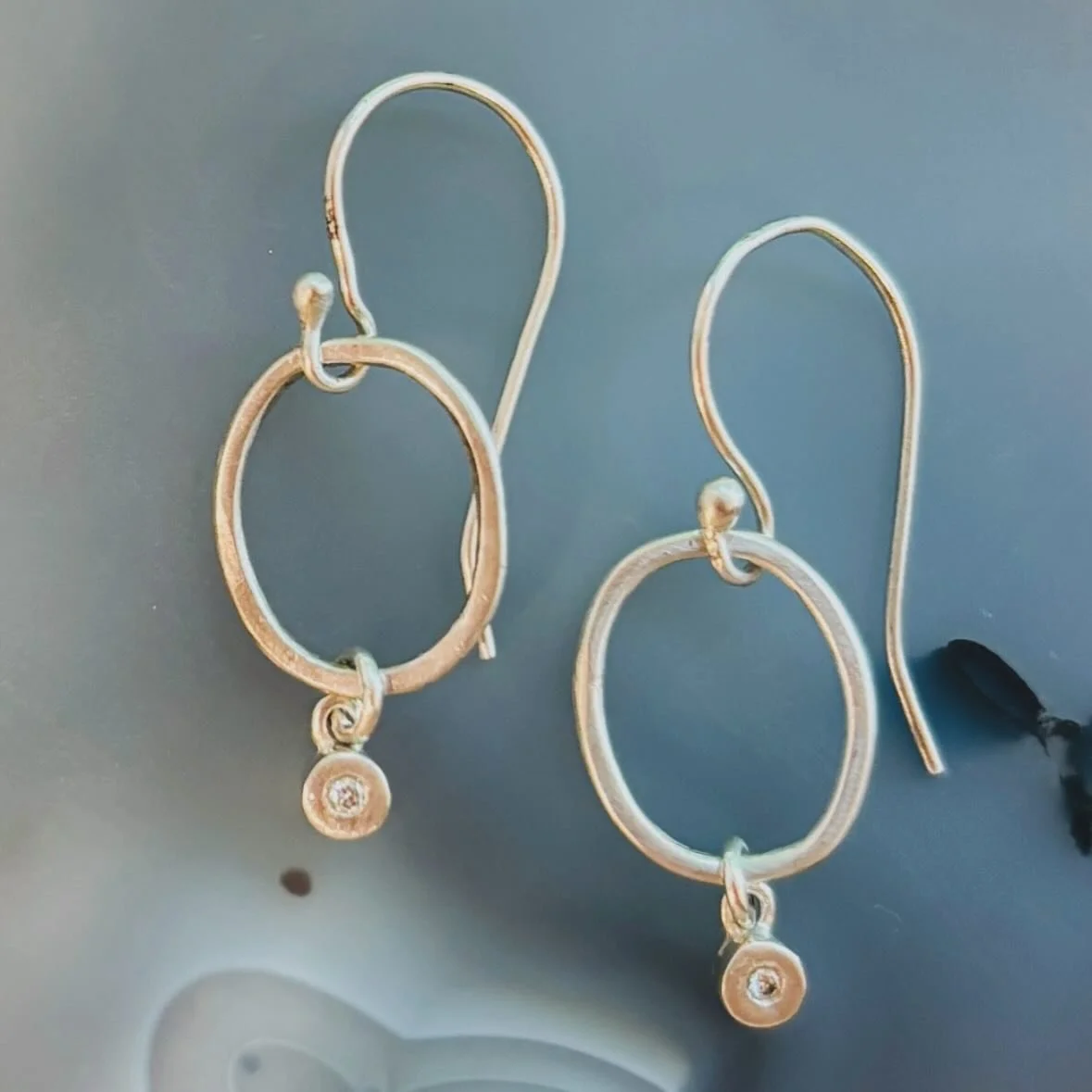 Elegant and effortless, these silver earrings feature a sleek oval design with a single diamond set in a delicate bezel, gently dangling below. The subtle sparkle of the diamond adds just the right touch of shine, making them a versatile piece that c