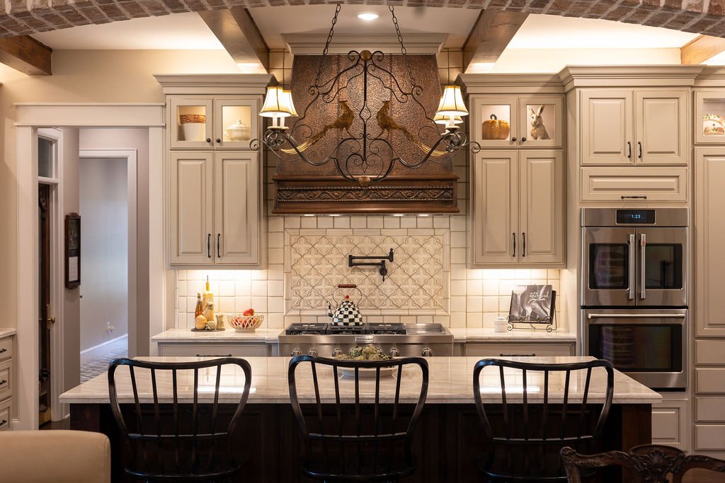 Kitchen with beige cabinetry, hand crafted tile backsplash, stainless steel double oven, decorative chandelier, and copper range hood.