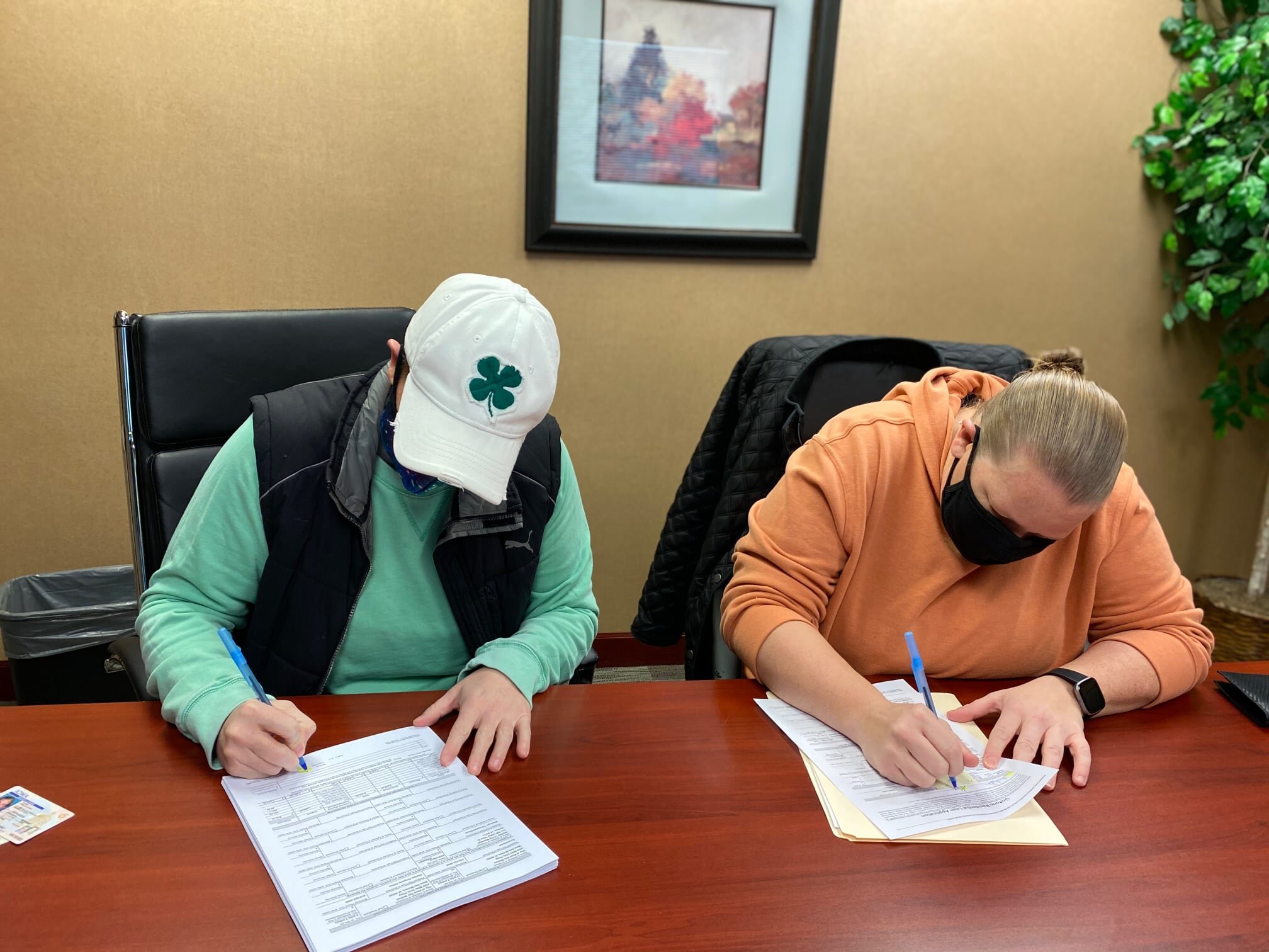 Two people sitting at a table, signing documents.