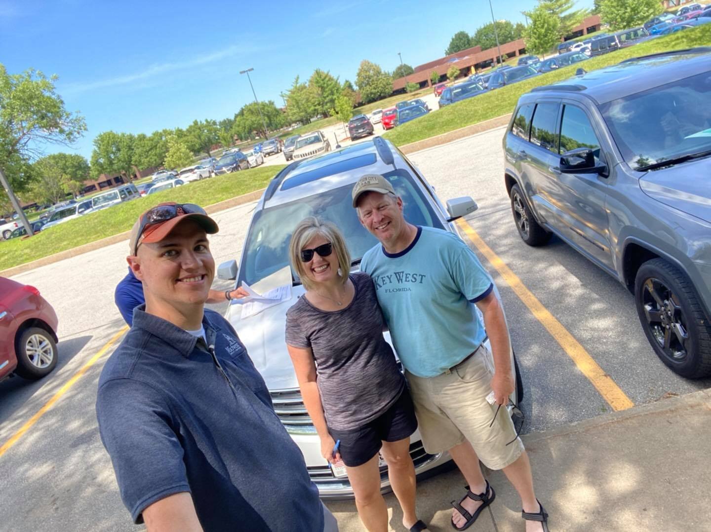 Three people standing outside of car, smiling.