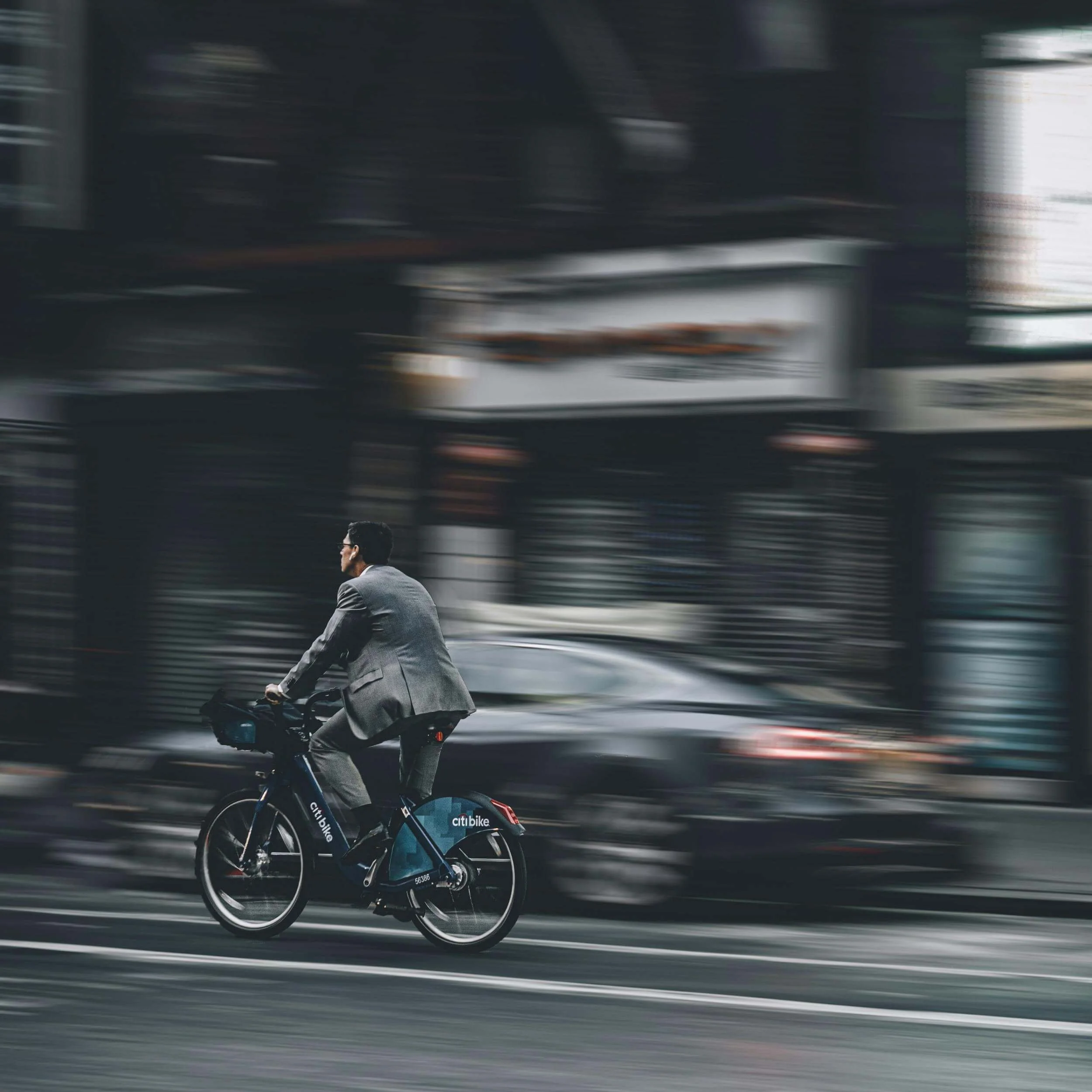 a man in a suit on a citi bike riding through a city