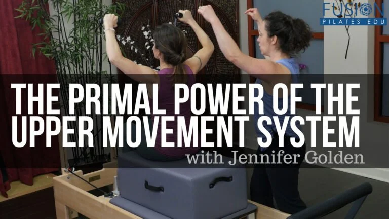 Two women practicing upper body movements on Pilates equipment in a studio with a banner titled 'The Primal Power of the Upper Movement System with Jennifer Golden'.