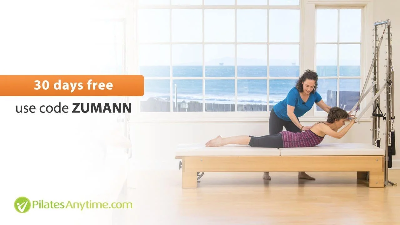 A woman practicing Pilates with the assistance of Jennifer Golden in a bright studio overlooking the ocean.