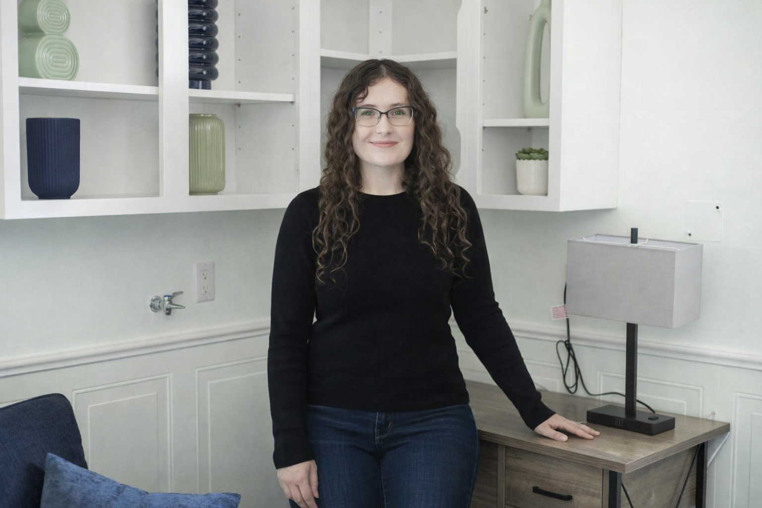 Racquel Devison stands in her office while wearing glasses and a dark sweater with one hand leaning on a table