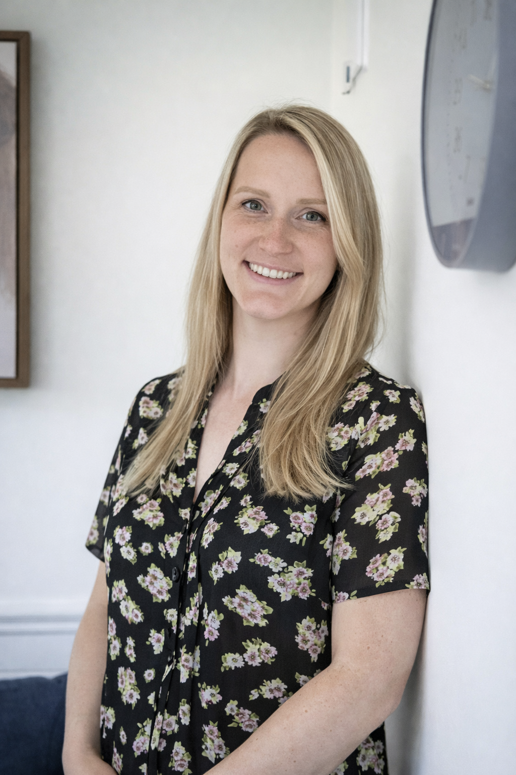 Stephanie Dagg smiles while leaning against the office wall while wearing a black and floral patterned outfit