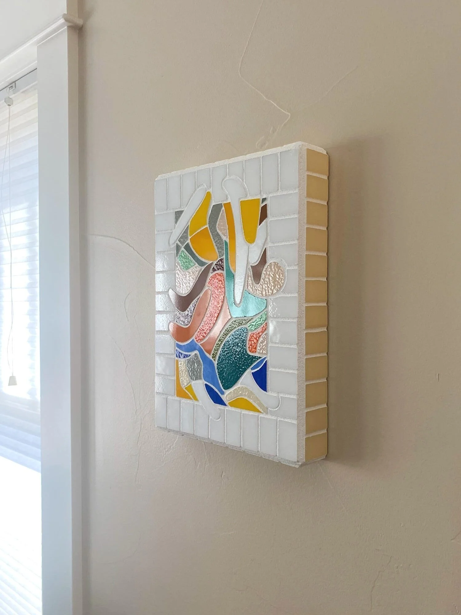 Abstract glass mosaic wall art by Ann Weinheimer hanging beside a window
