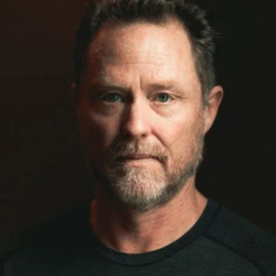 Portrait of a man with a beard and dark shirt against a dark background.
