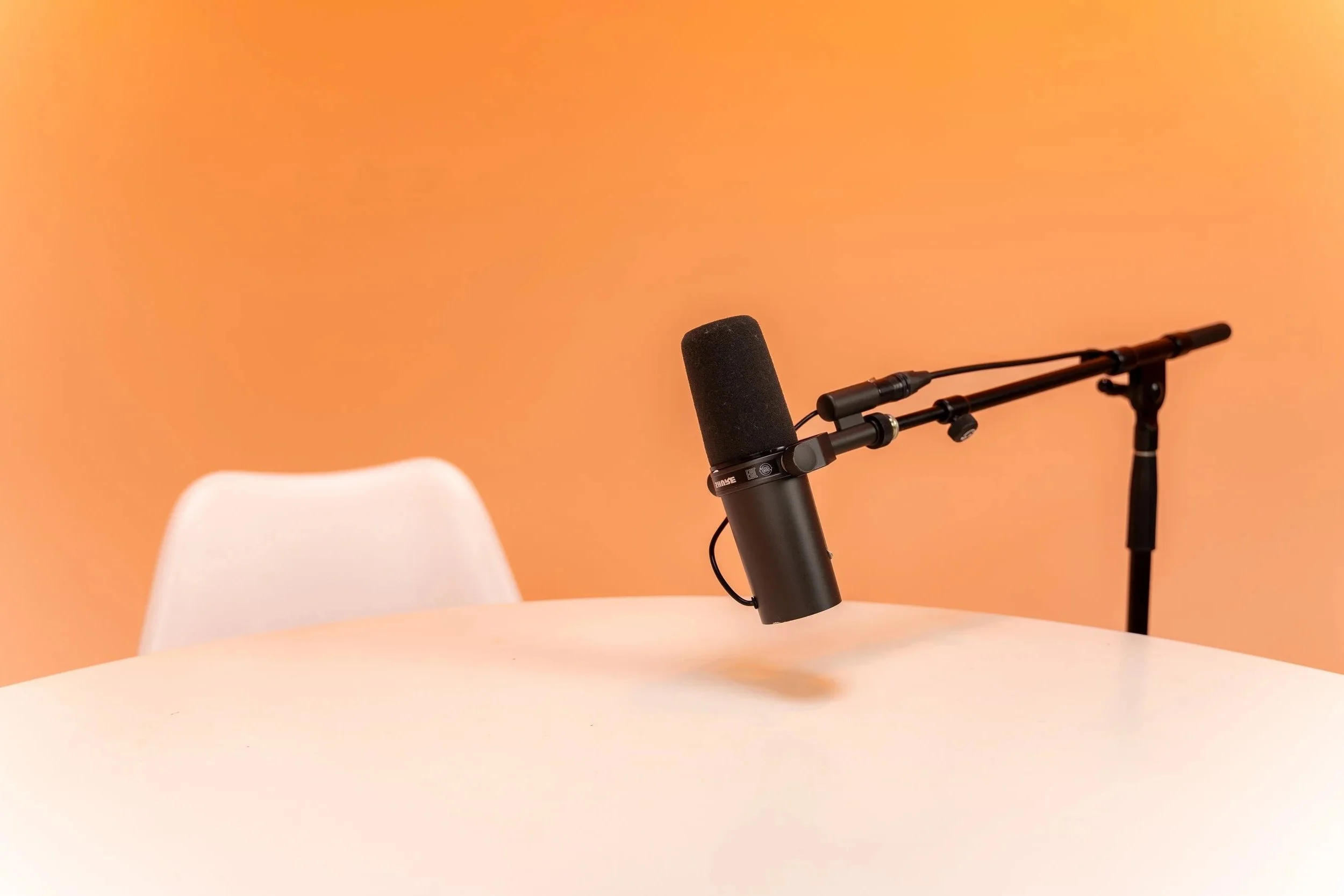 Microphone mounted on a stand over a white table with a white chair in the background, against a peach-colored wall.