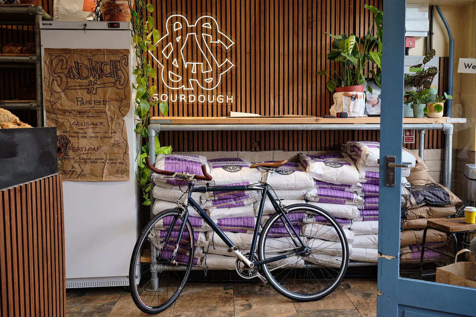 Inside a coffee shop a bike is resting on some bags of flour