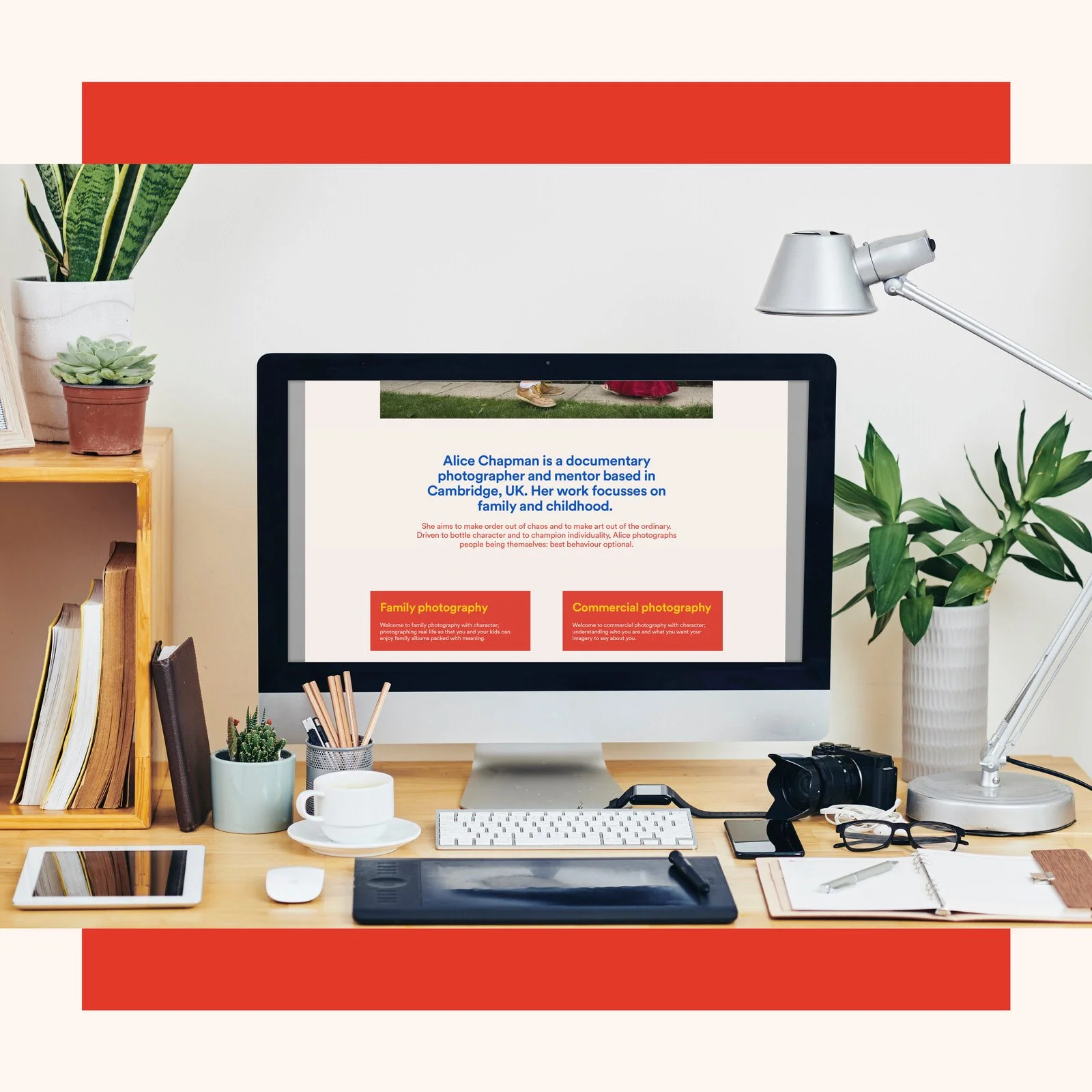 An organized workspace with a computer, various plants, a camera, books, notebooks, and office supplies on a wooden desk.
