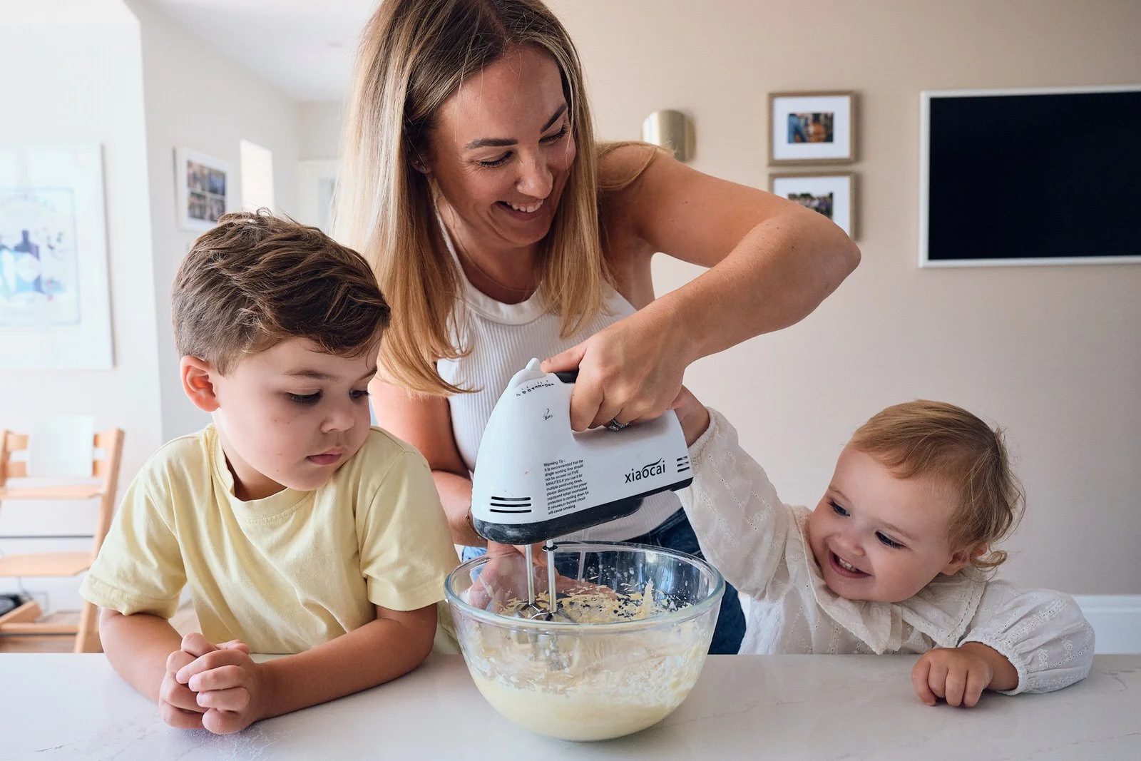Mother baking. inteh kitchen with her 2 children using a whisk