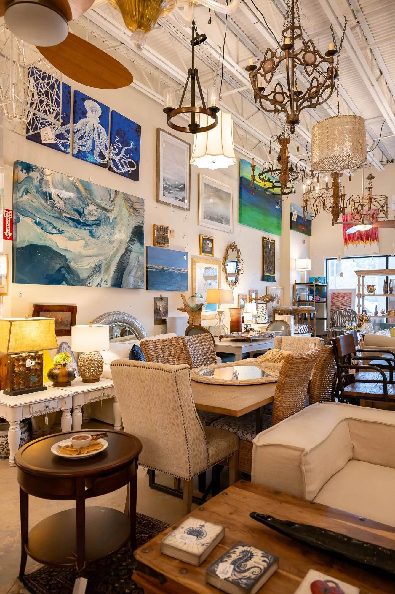 Interior of a furniture and home decor store featuring various paintings on the wall, chandeliers hanging from the ceiling, and a variety of chairs and tables