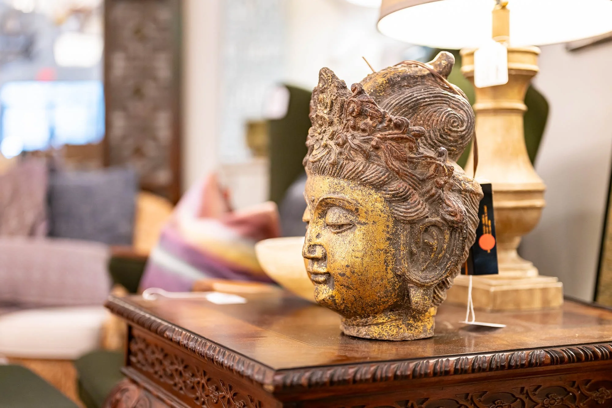 An intricately carved bust of a woman with detailed hair and facial features, vintage gold finish, placed on a wooden table in a store or antique shop.