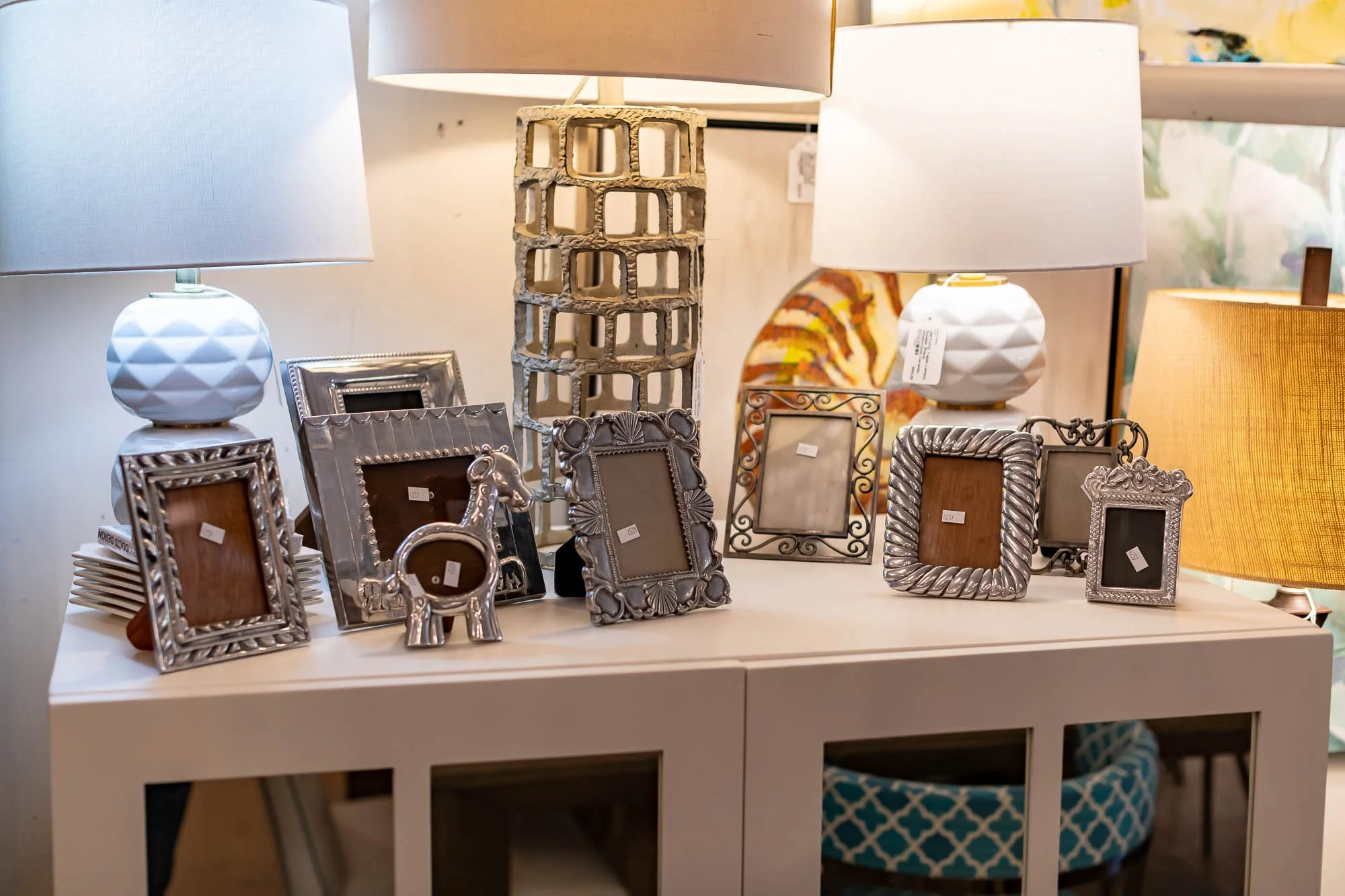 A collection of decorative picture frames, ceramic table lamps, and a small decorative horse figurine on a white table in a store.