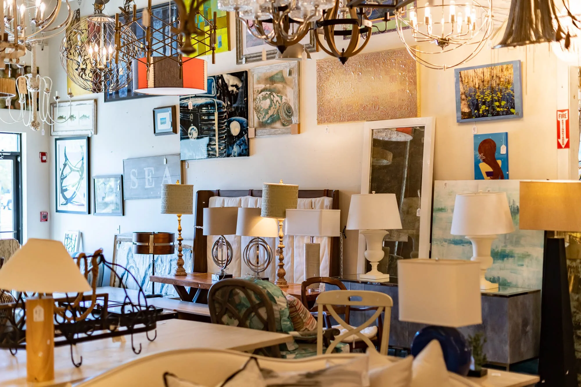 Interior of an art and furniture store with various lamps, chandeliers, framed artwork on the walls, and furniture pieces.