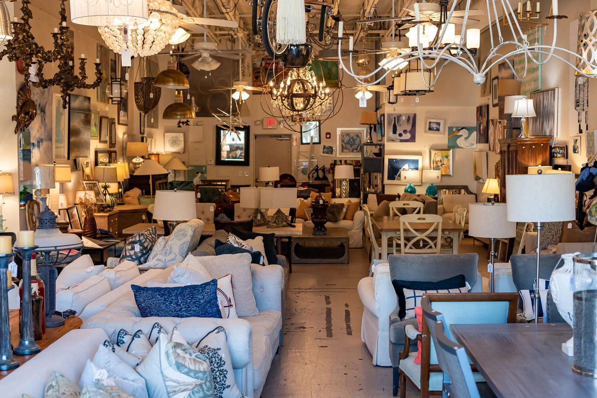 Interior of a furniture store with various sofas, chairs, and lamps, and a ceiling filled with multiple different chandeliers and light fixtures.