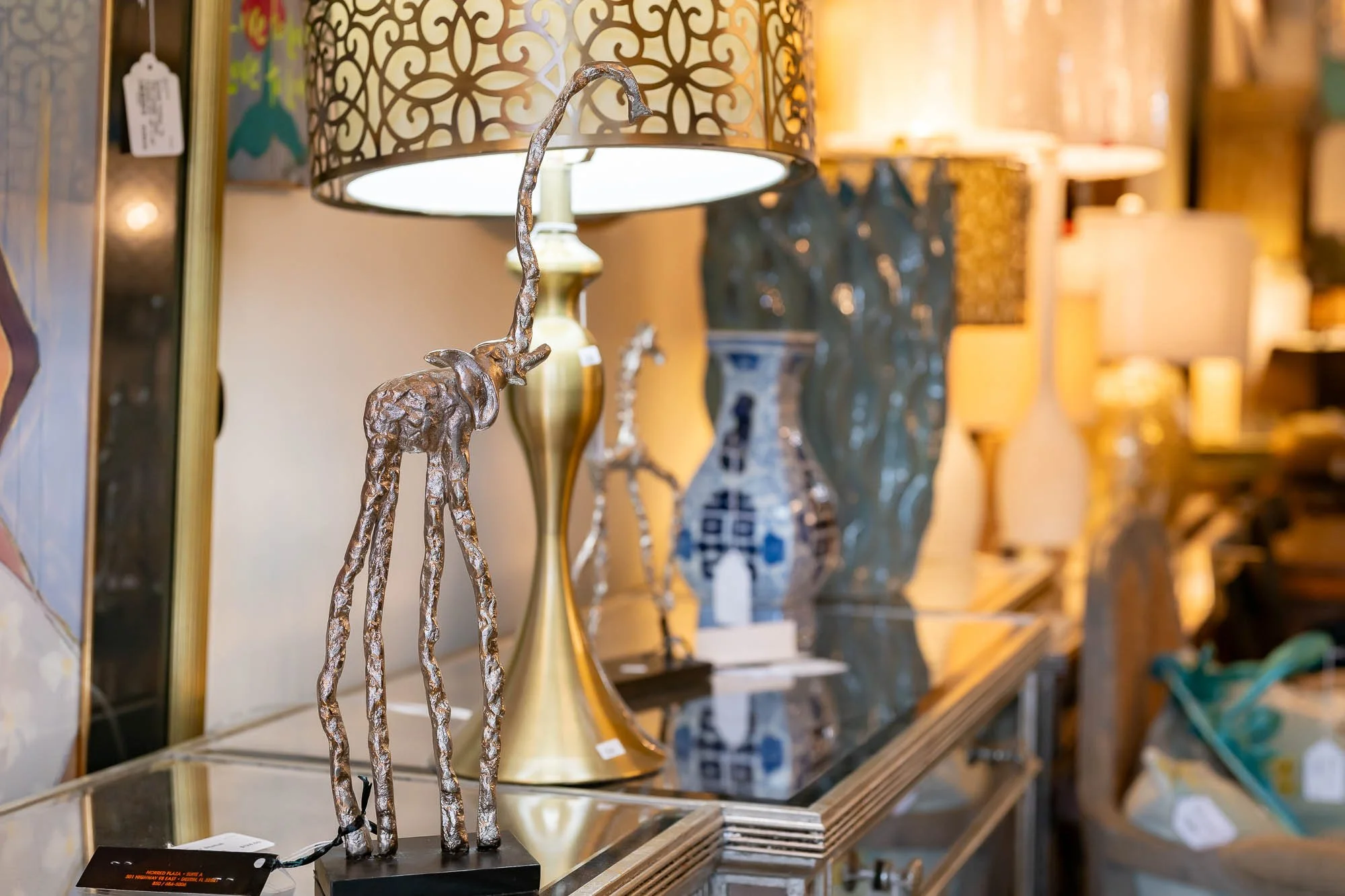 A decorative silver giraffe sculpture in front of a table with various lamps and vases in a store.