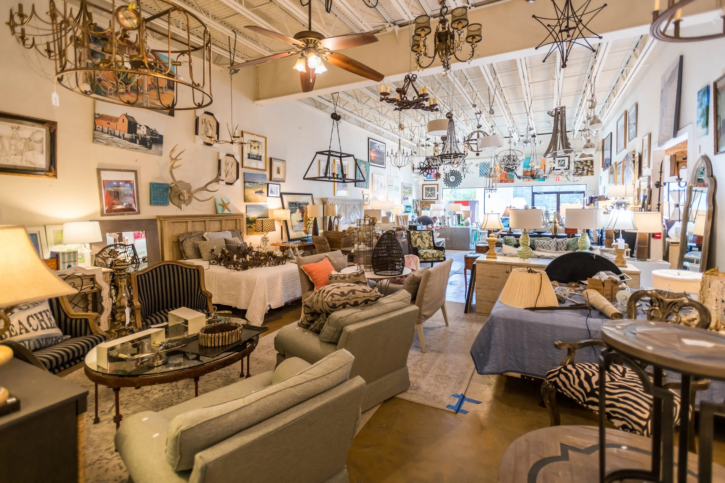 Interior of a vintage furniture and home decor store with various sofas, tables, lamps, artwork, and hanging chandeliers and light fixtures.