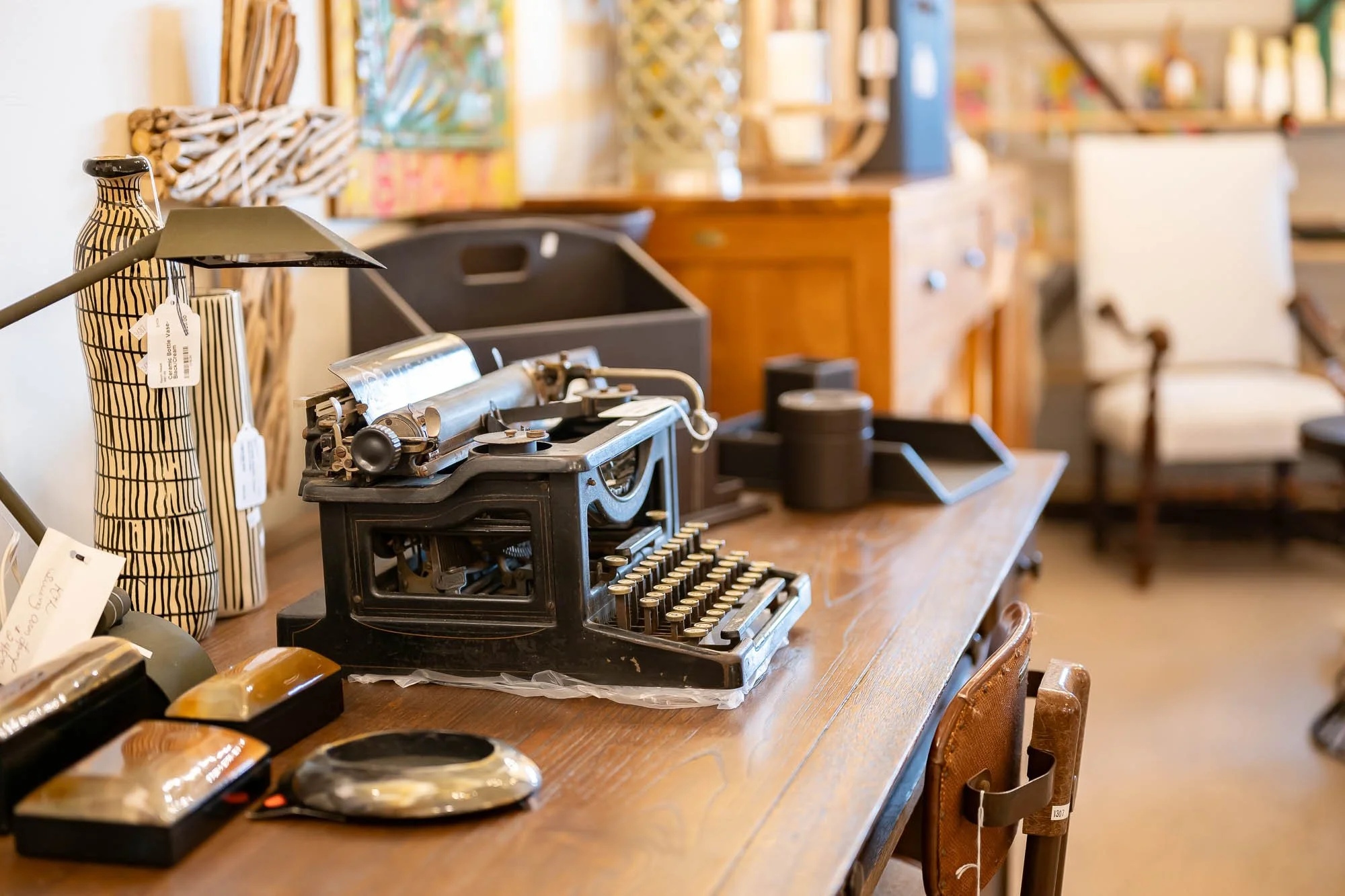 Vintage typewriter on a wooden table surrounded by decorative items and furniture in a cozy vintage shop.