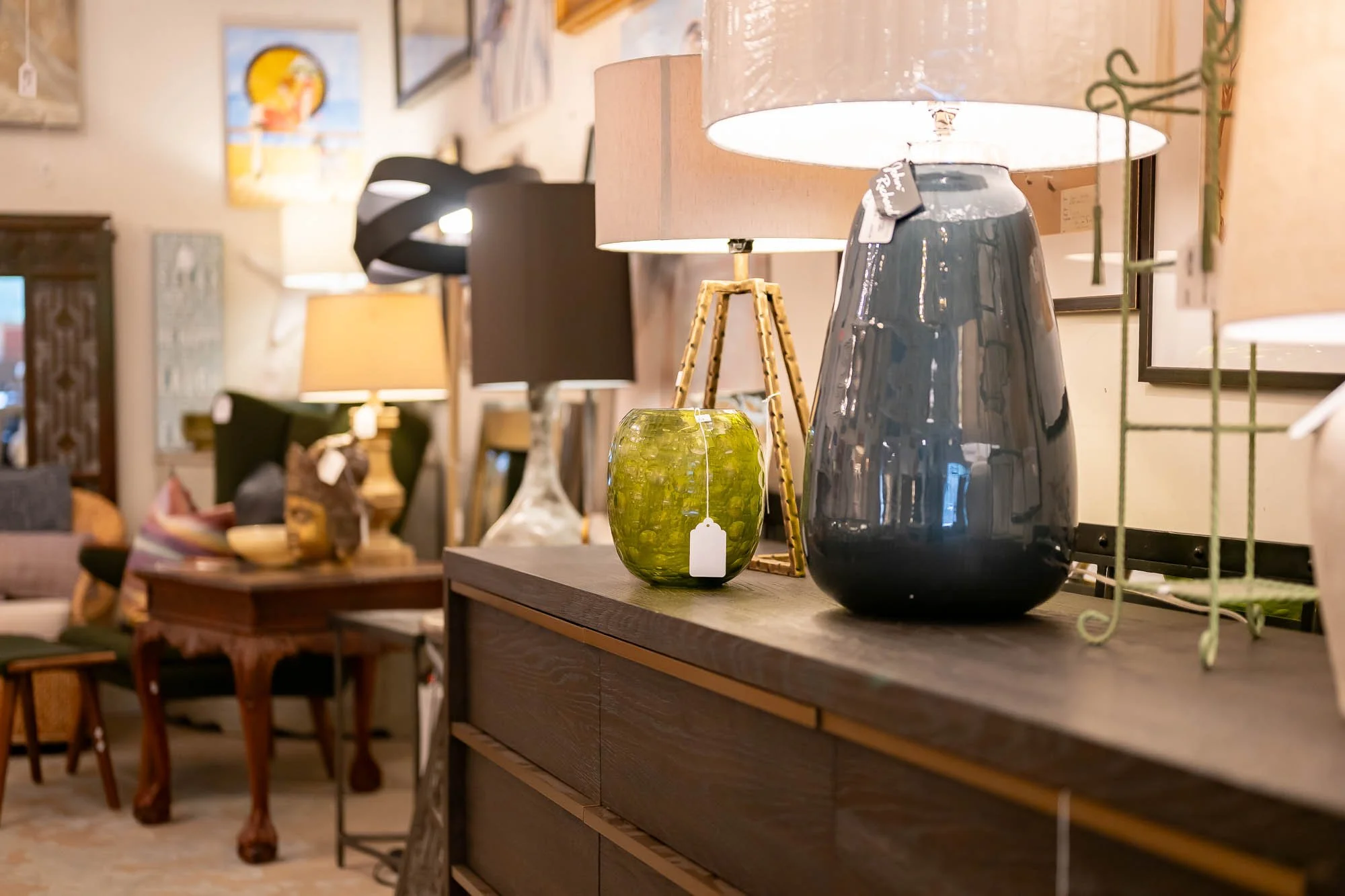Decorative lamps on a wooden sideboard in a furniture store, with various other lamps and furniture in the background.