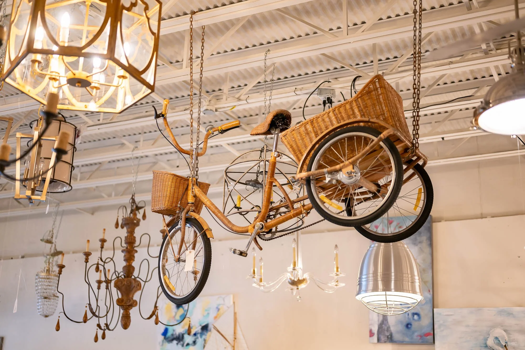 Decorative ceiling display with an old-fashioned bicycle with woven baskets hanging from the ceiling, surrounded by chandeliers and hanging lamps.