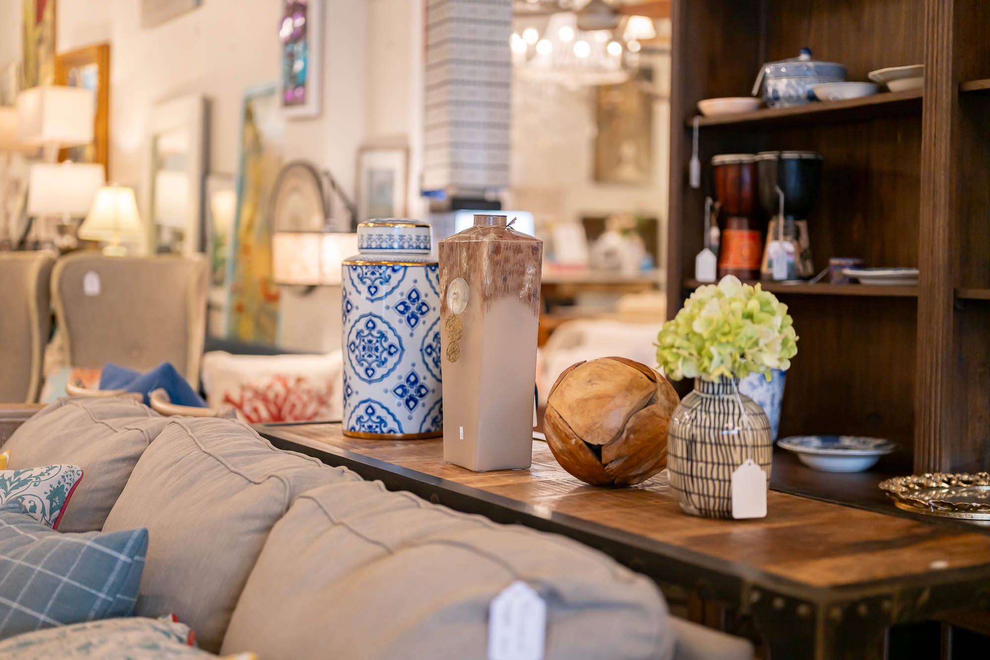 Decorative vases and a wooden sculpture on a wooden table in a furniture store, with various furniture and lamps in the background.