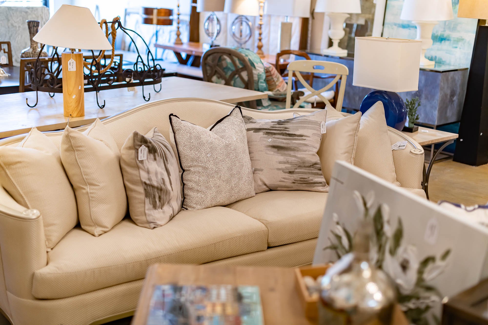 A beige sofa with five decorative pillows, in a store with various lamps and furniture.