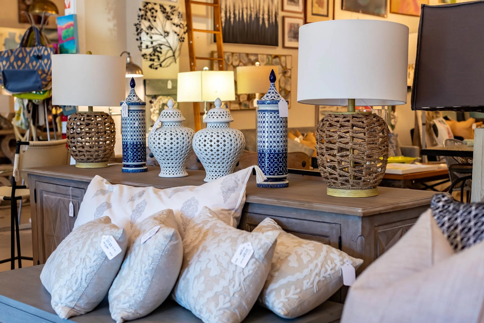 Display of lamps and decorative pillows on a wooden table in a home decor store.