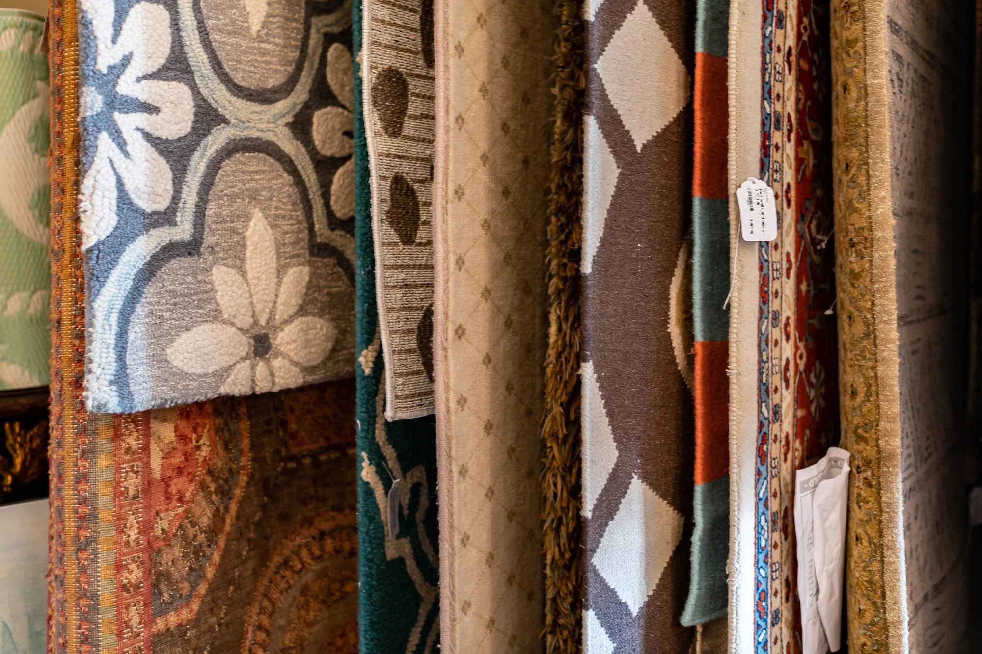 Multiple rolled and folded area rugs with various patterns and colors, displayed on a surface.
