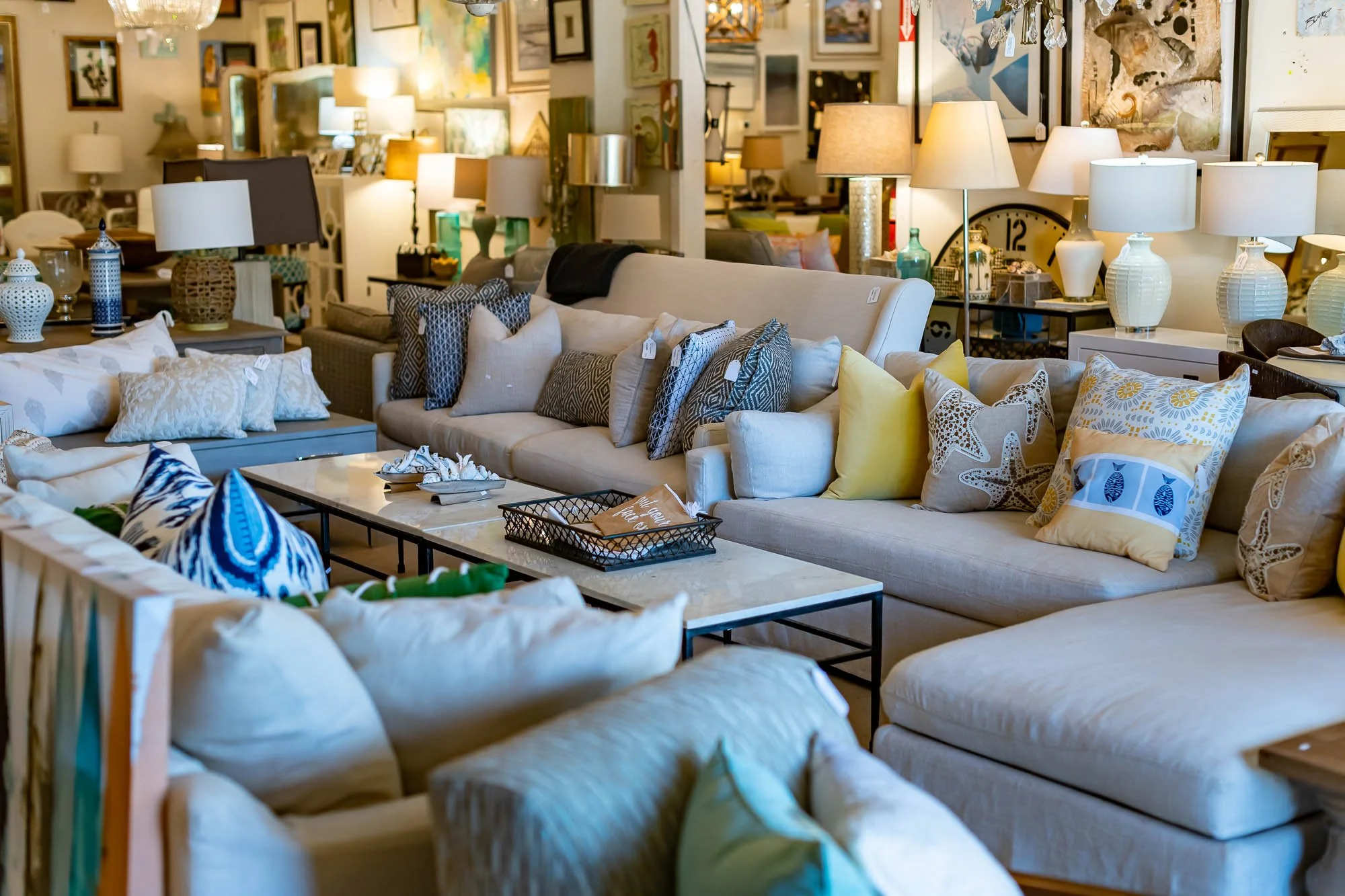 Furniture store display with a variety of sofas, armchairs, and side tables, adorned with decorative pillows and lamps, in a well-lit setting.