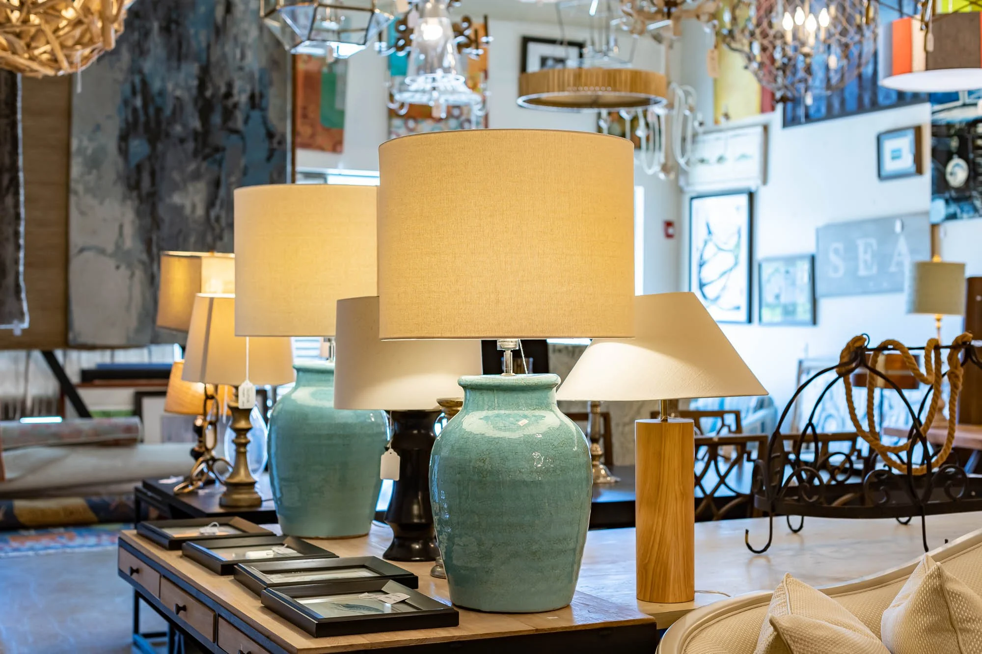 Assorted table lamps displayed on a wooden table inside a furniture or home decor store.