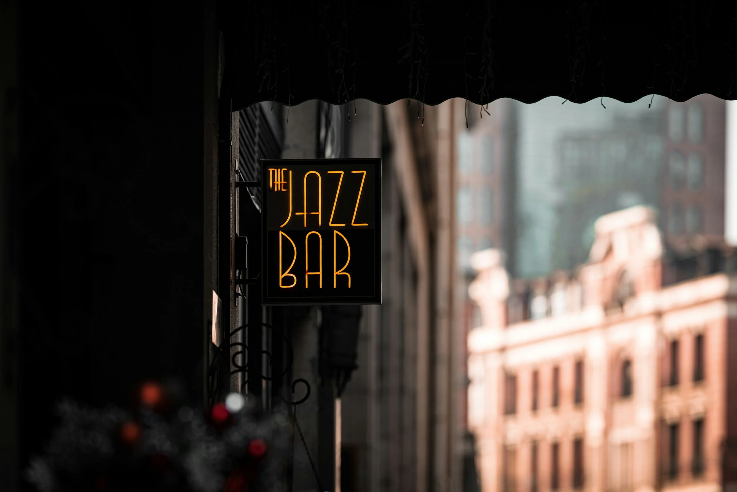 Neon sign reading 'The Jazz Bar' hanging outside a building on a city street in the daytime