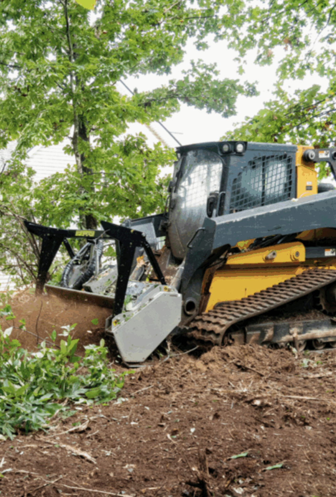 A bulldozer clearing soil with a green leafy tree in the background.