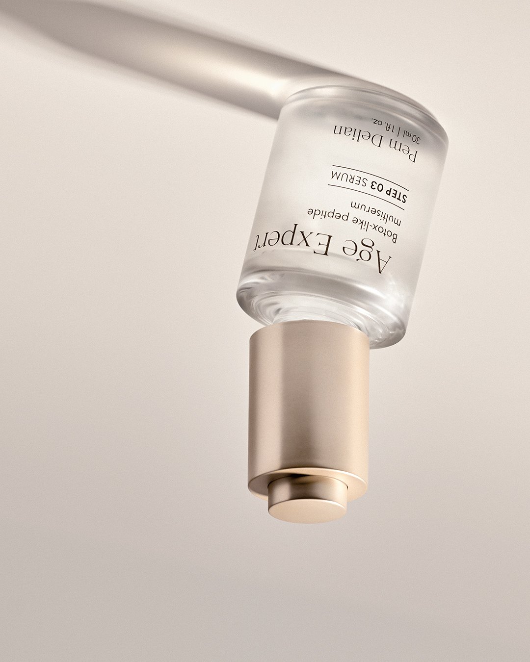 Pem Delian Age Expert peptide serum bottle held upside down, showing gold cap and label detail.