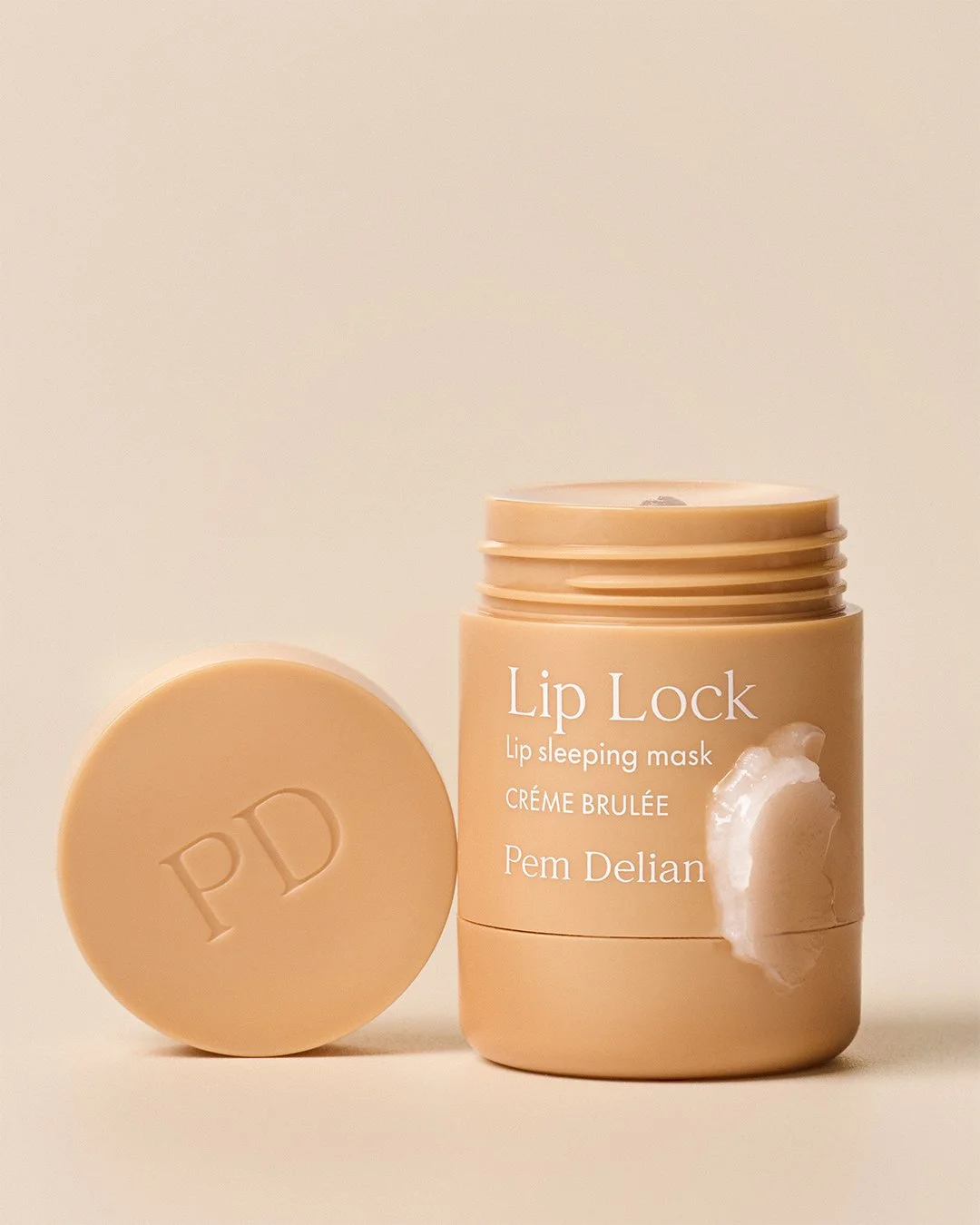 Open jar of Pem Delian Lip Lock Créme Brulée lip sleeping mask with balm swatch and "PD" lid.