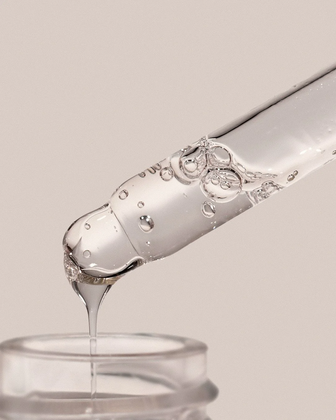 Clear anti-aging peptide serum dripping from Pem Delian Age Expert dropper into the bottle.