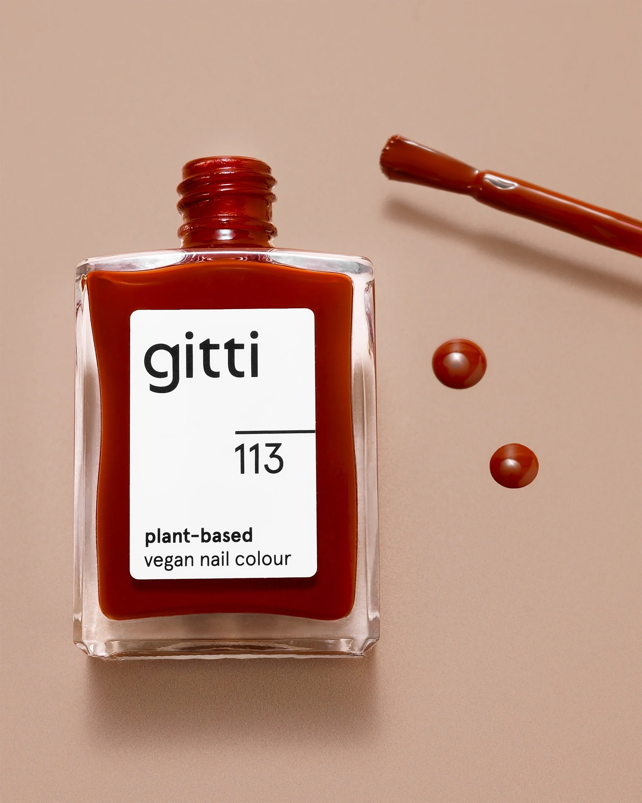 Open bottle of Gitti 113 nail polish with glossy product drops on nude background. Clean commercial texture photography showing formula and finish.