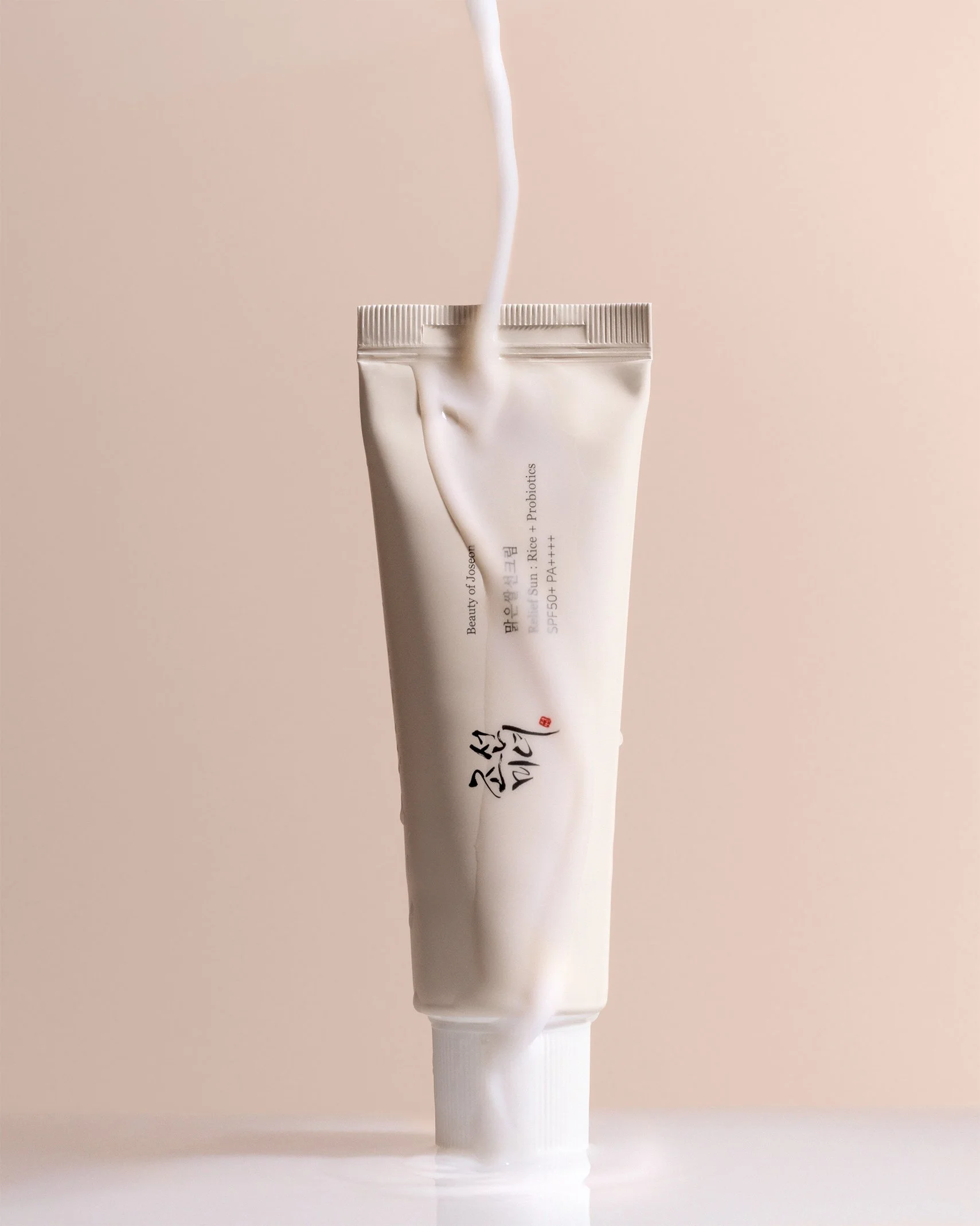 Beauty of Joseon Relief Sun Rice + Probiotics SPF 50+ sunscreen tube with cream pouring over it on blush background