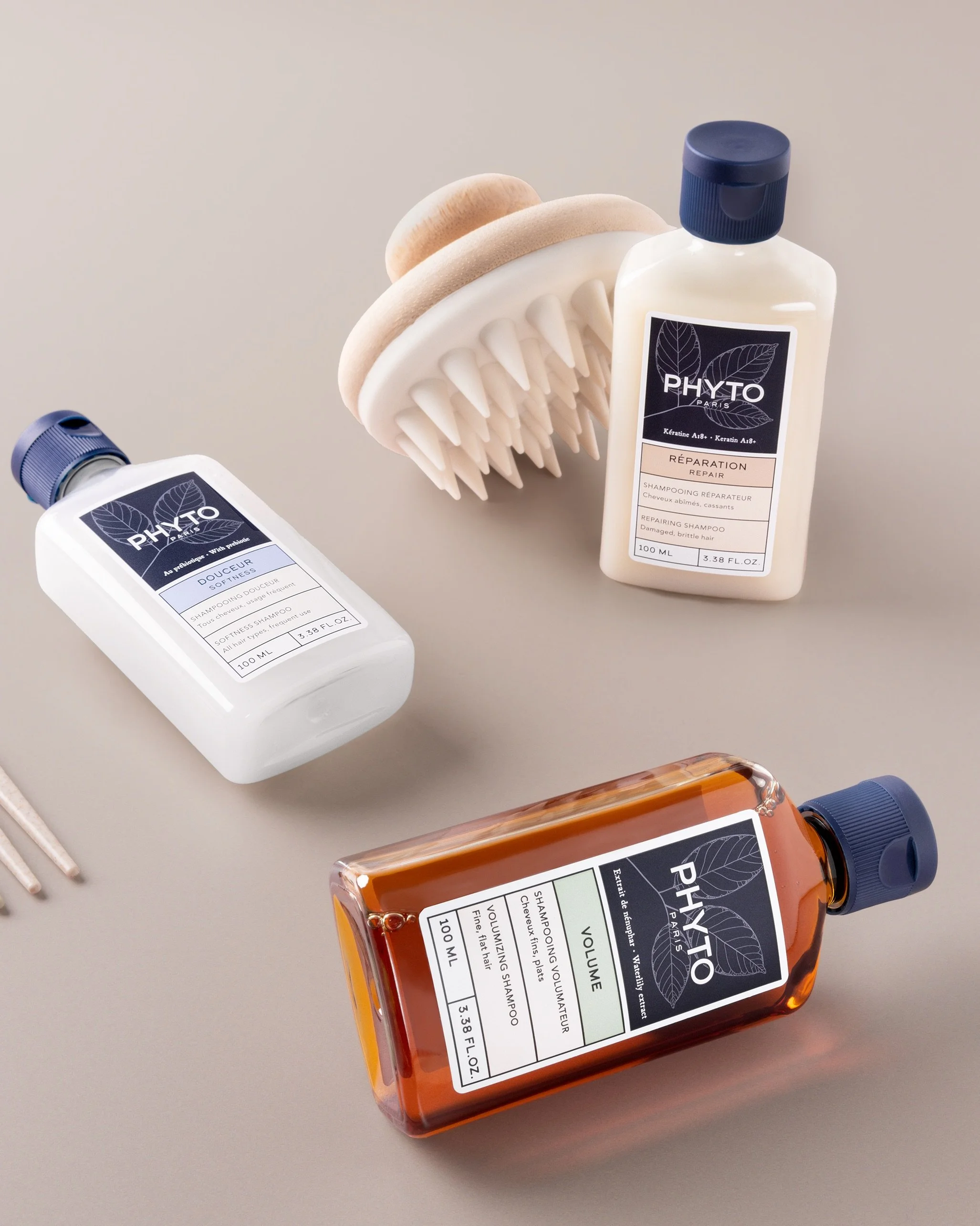 Minimal flatlay of three Phyto Paris shampoo bottles in soft neutral tones with a wooden scalp brush, styled in natural light.