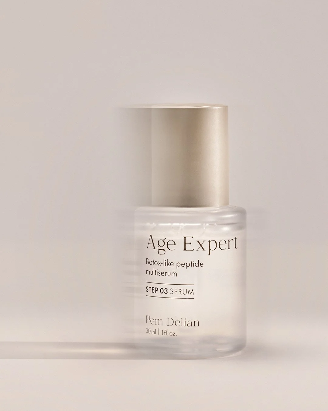 Pem Delian Age Expert peptide serum bottle with gold cap and soft shadow on beige background.
