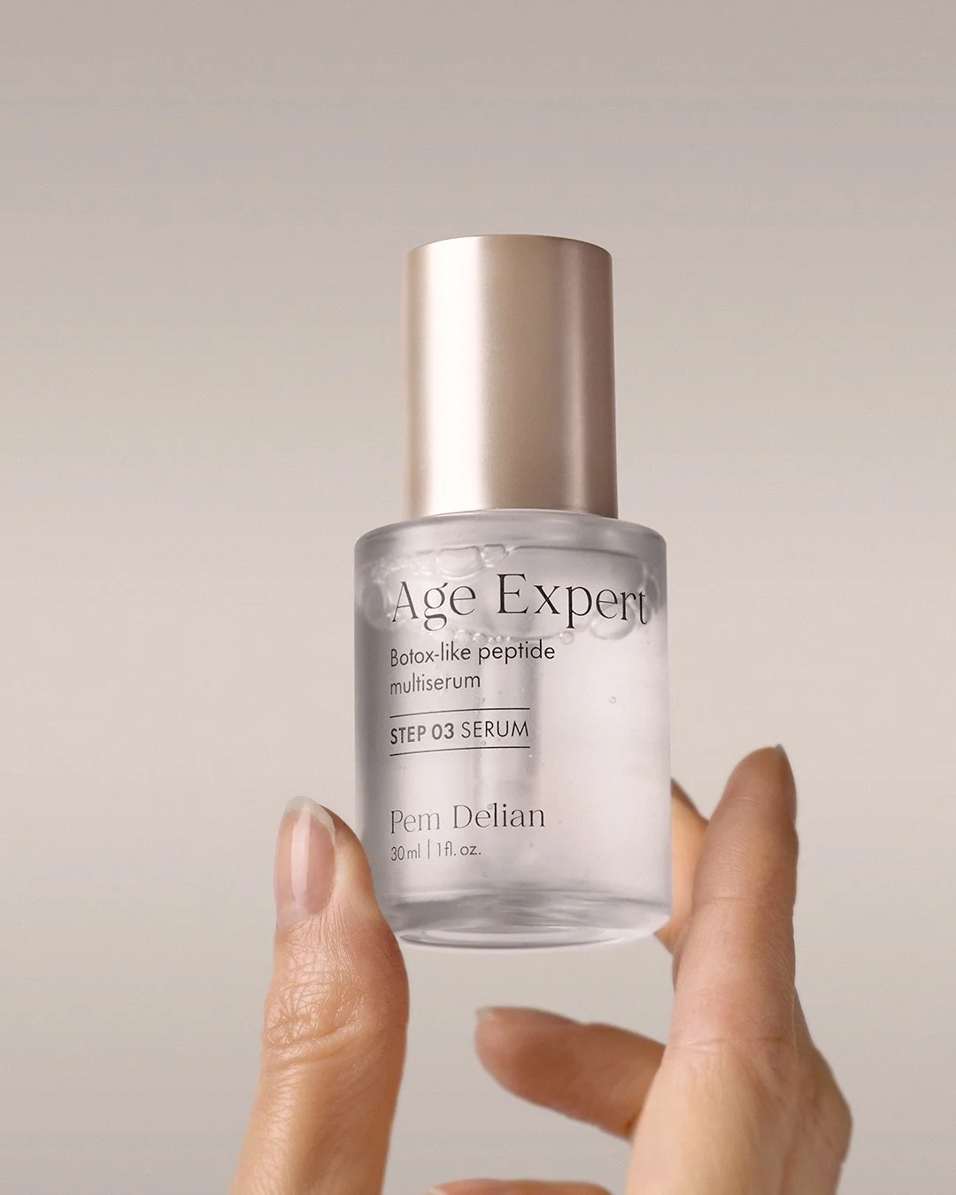 Hand holding Pem Delian Age Expert peptide multiserum bottle to show size and gold cap detail.