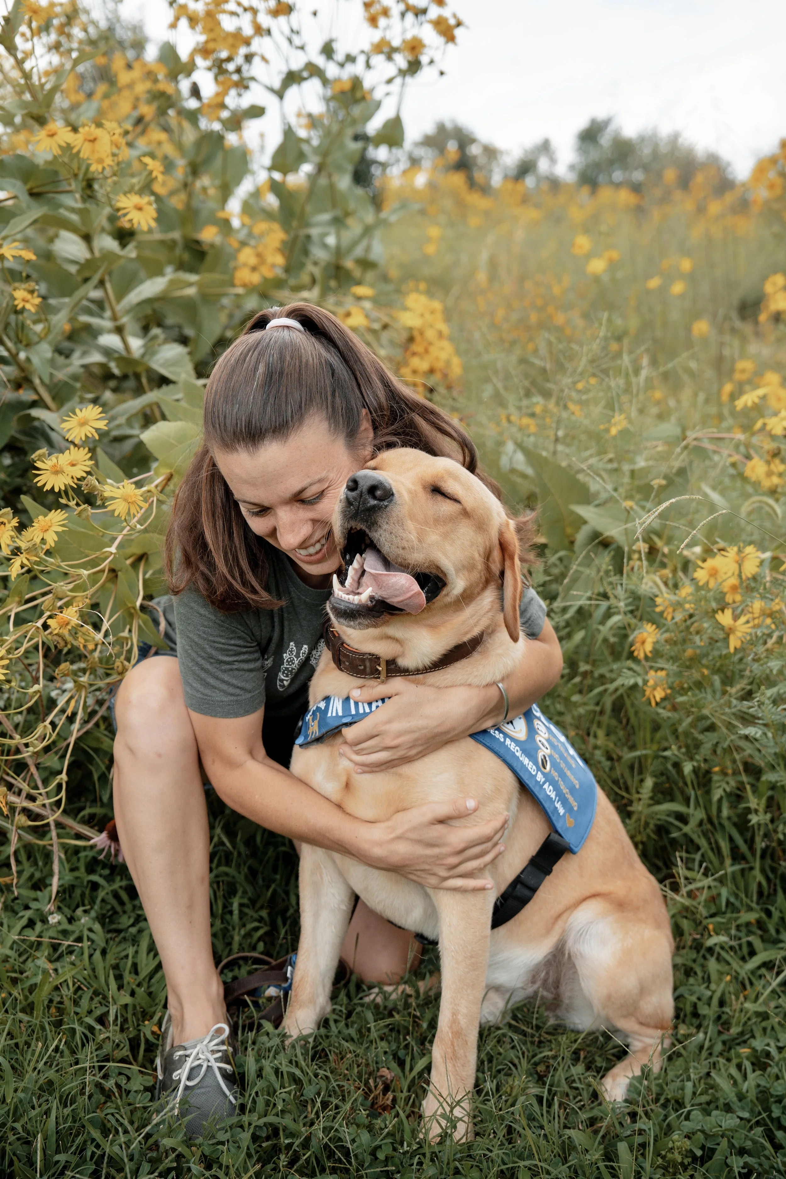 A woman hugging a happy Labrador retriever dog in a field of yellow flowers.