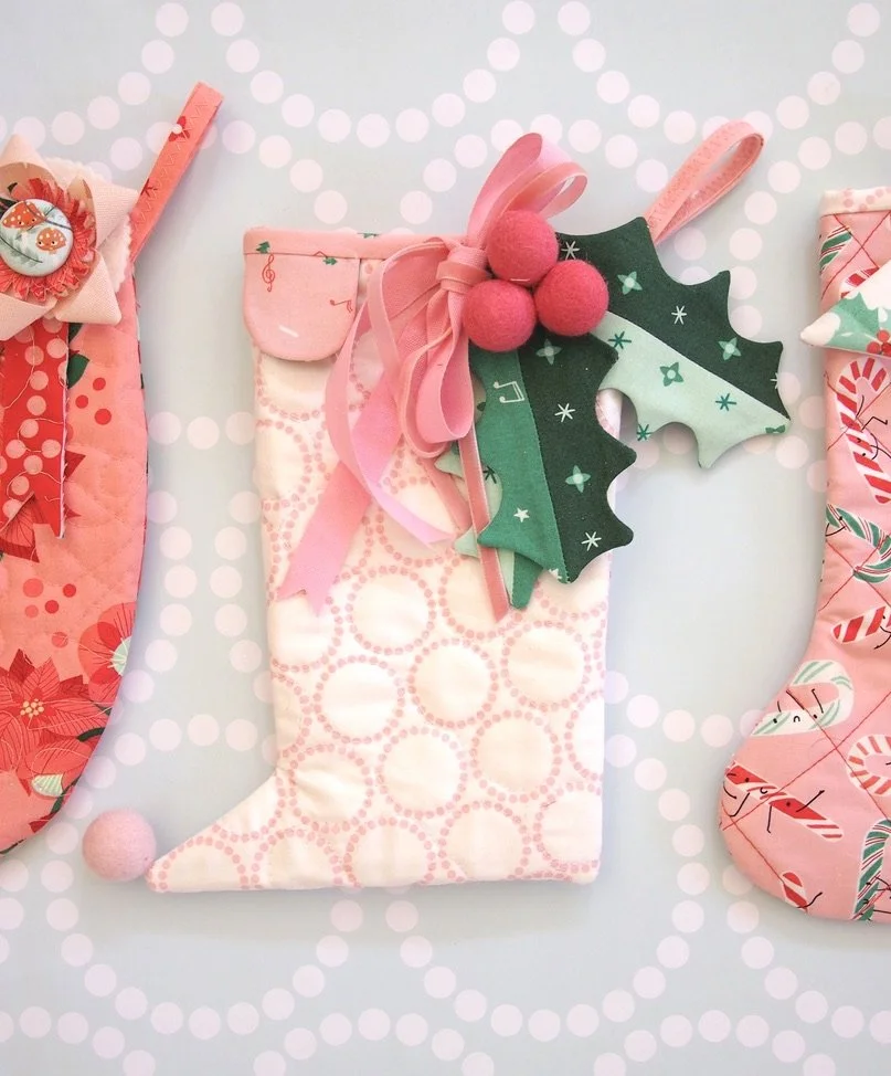 Pink Christmas stocking with holly leaves, pink pom-poms, ribbons, and festive decorations on a light background with a dotted pattern.