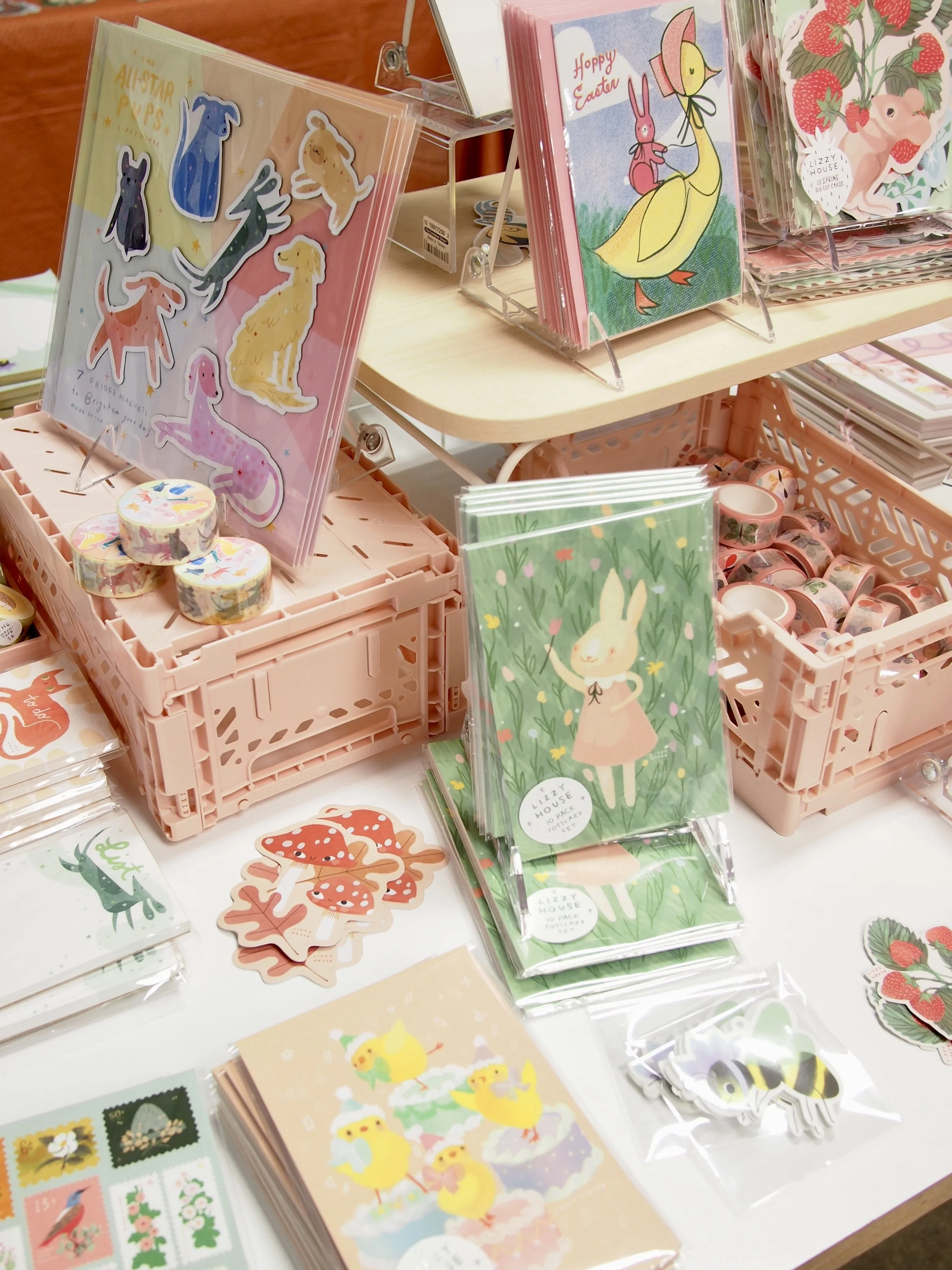 Display of colorful Easter-themed greeting cards, stickers, and postage stamps with designs of bunnies, ducks, and strawberries arranged on a table at a store.