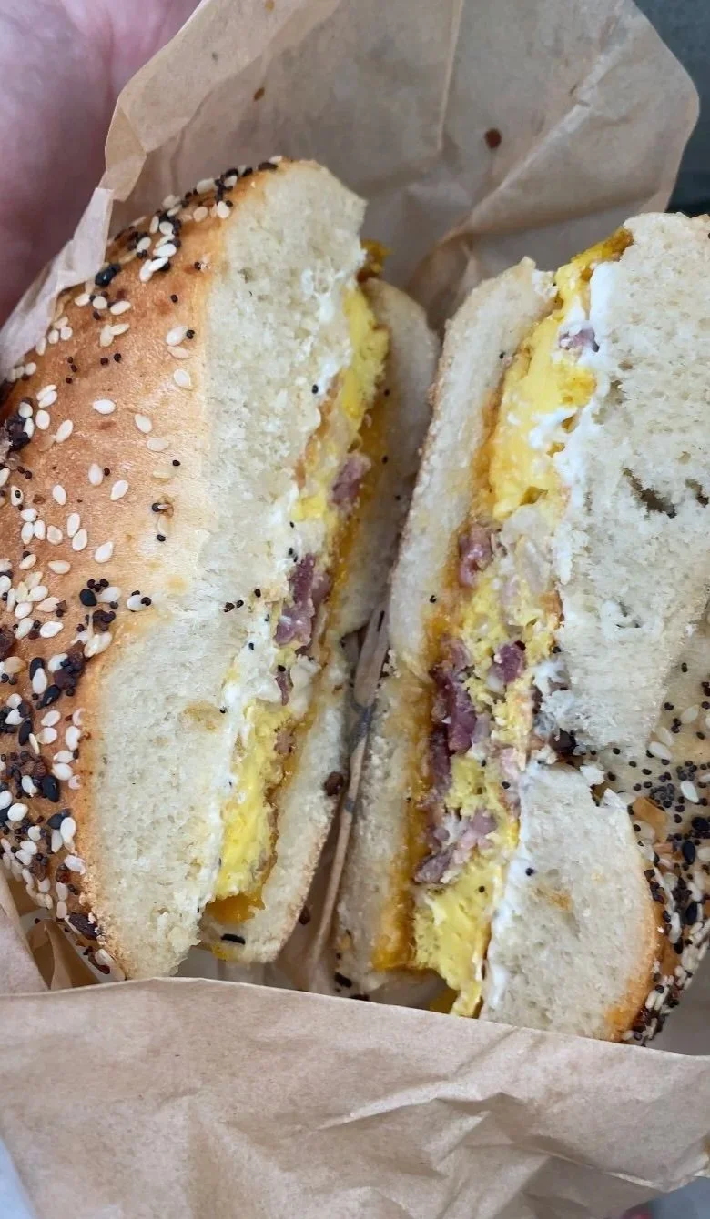 Close-up of a sandwich with scrambled eggs and ham on a sesame seed bun, wrapped in paper