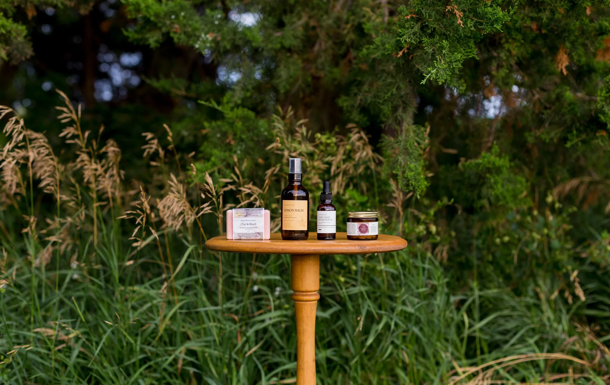 Meadowlark Made's simple 4 step skincare routine on a wooden stand with grasses and trees in the background