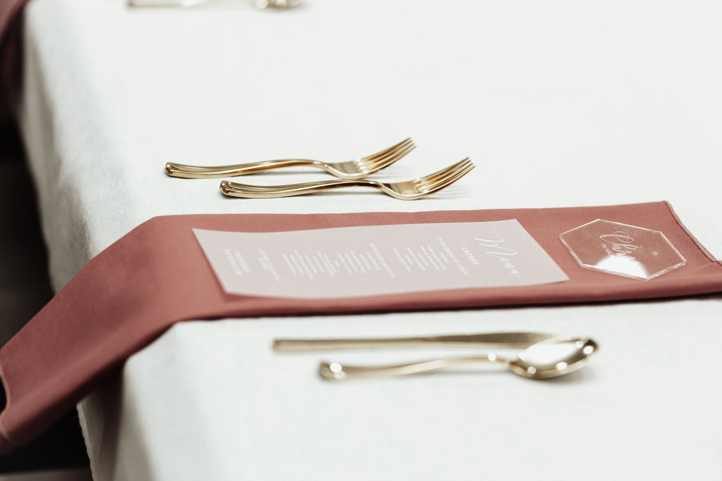 Set of gold cutlery on a white table with a pink napkin and a menu card.