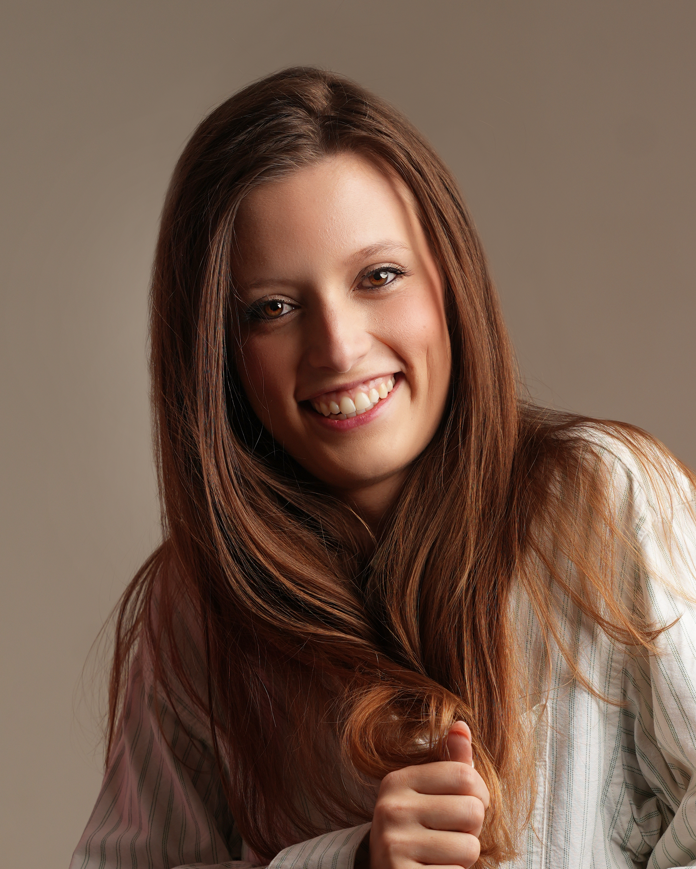 Young woman with long brown hair smiling and wearing a white striped shirt.